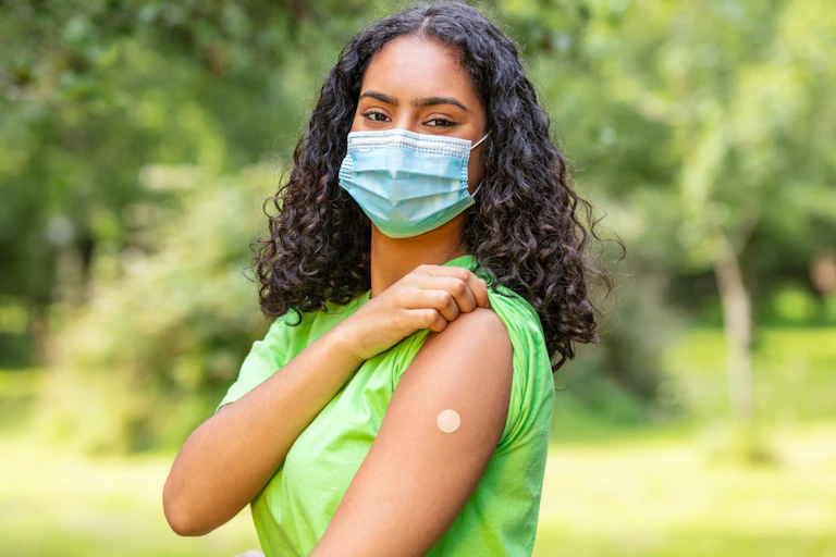 Teenager wearing mask showing vaccination plaster or bandaid on upper arm
