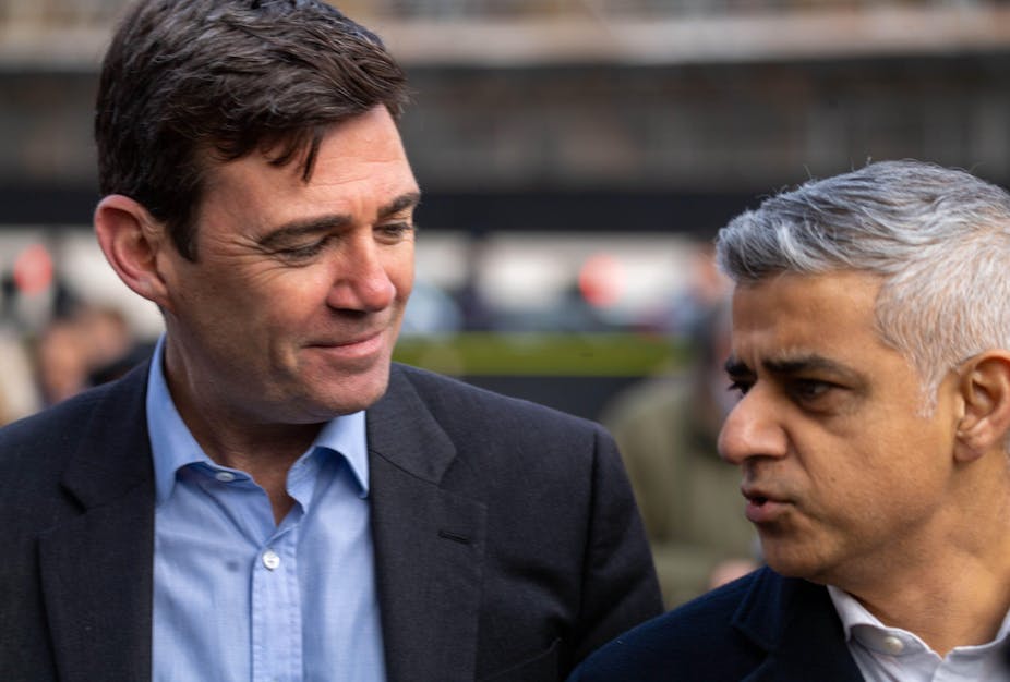 Close-up photo of Andy Burnham looking at Sadiq Khan as both mayors attend an event