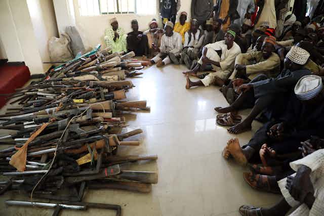 Men siiting on the floor and looking at a stash of seized guns