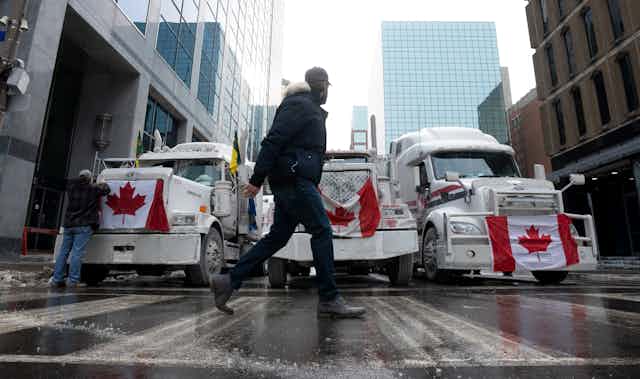 A person walks past trucks draped with Canadian flags parked on a city street.