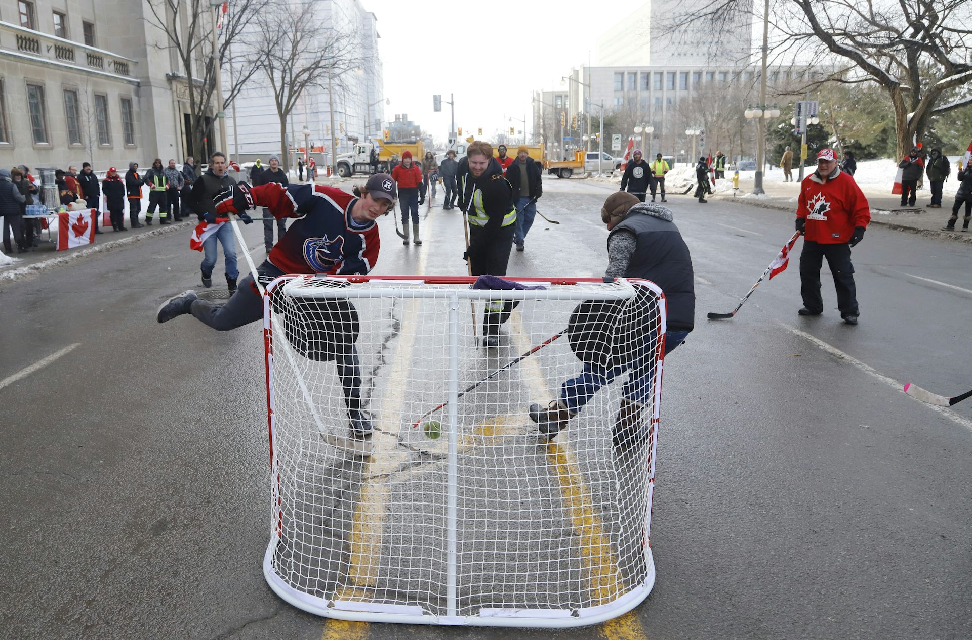 Men play street hockey on a wide city street.