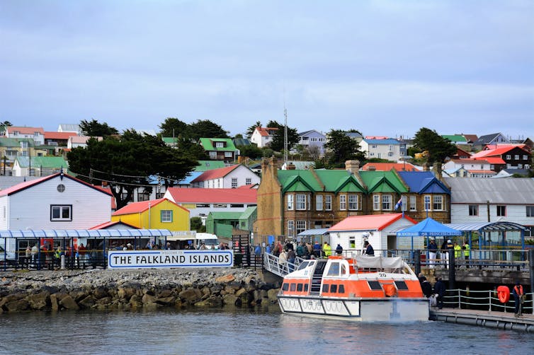 An orange tender boat brings visitors ashore from a cruise boat.