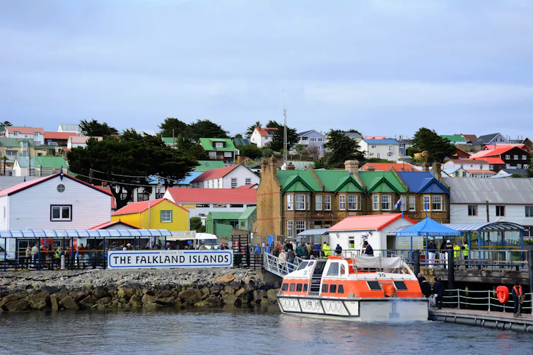 An orange tender boat brings visitors ashore from a cruise boat.