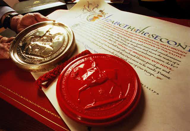 A man holds a solid silver matrix next to a red seal on a piece of calligraphed parchment.