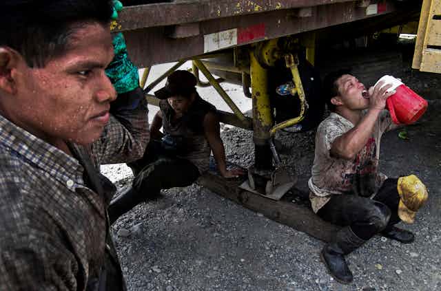 Three sweating workers find shade under a truck during a break.