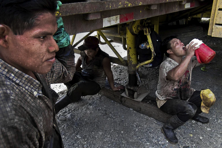 Three sweating workers find shade under a truck during a break.