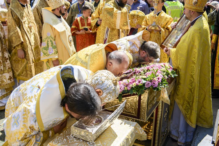 Members of the Ukrainian Orthodox Church dressed in religious regalia hold a service as people offer their prayers by bowing in front of them.