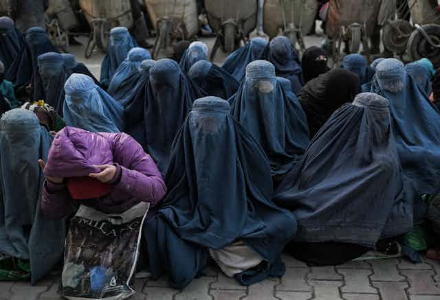 Several rows of seated women sit together, wearing blue burqas covering their entire bodies and faces.