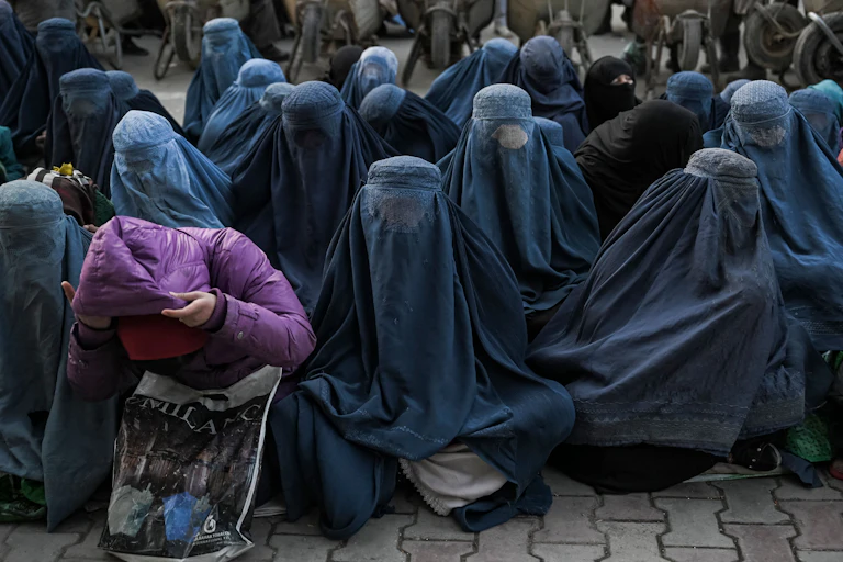 Several rows of seated women sit together, wearing blue burqas covering their entire bodies and faces.
