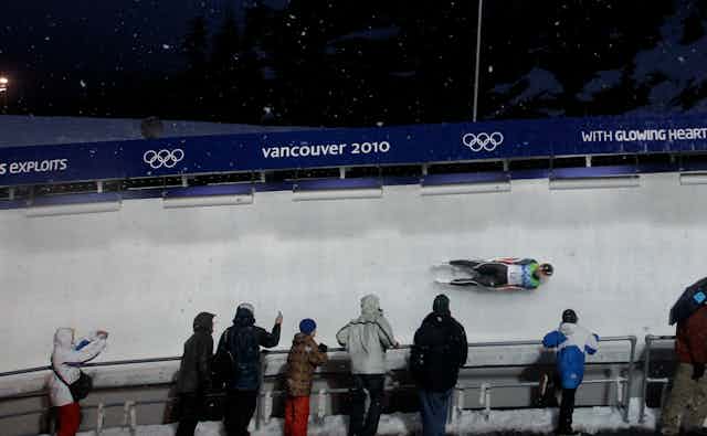 A luge racer going around a turn with fans by the side of the track.