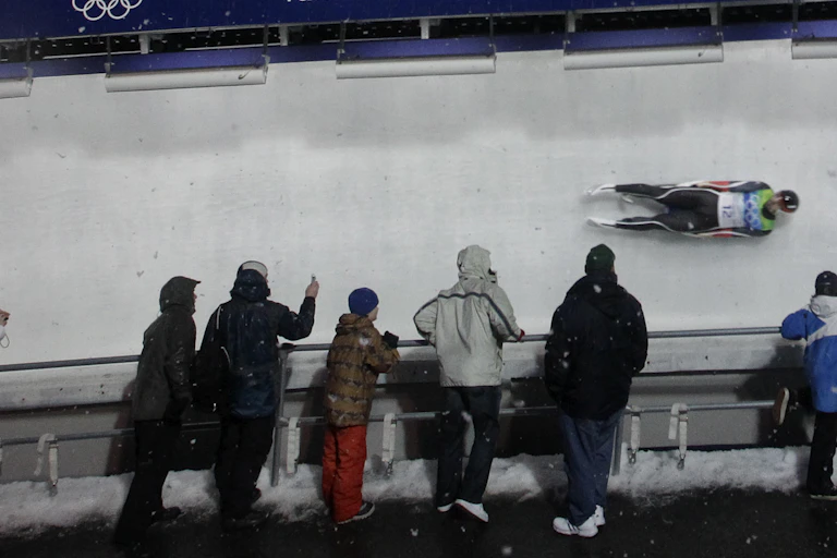 A luge racer going around a turn with fans by the side of the track.