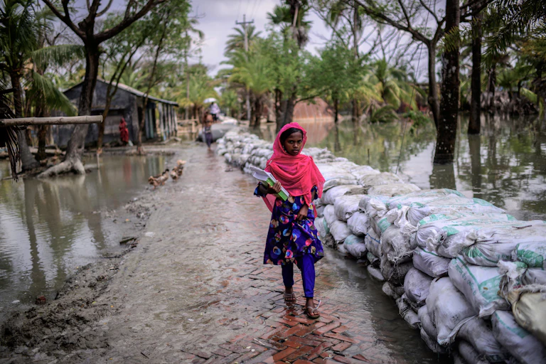 A student walks on a flooded brick road with sandbags on one side holding back water in 2021.