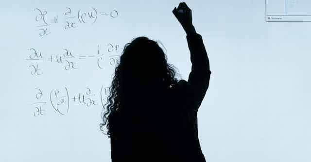 Silhouette of a professor seen writing math equations on a whiteboard.