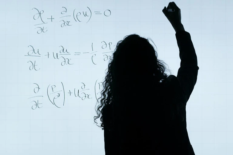 Silhouette of a professor seen writing math equations on a whiteboard.
