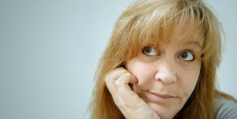 Woman with light-colored hair and dark eyes looking up and to the side, as if seeing her own thoughts, with her chin resting in her hand.