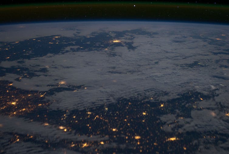 a view of earth from space at night with scattered clouds and city lights below them