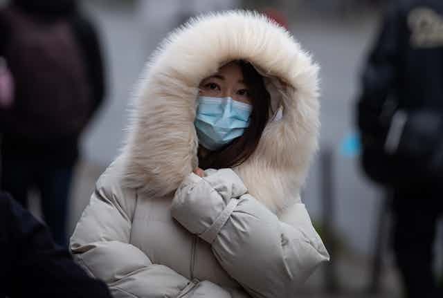 A person in a white winter jacket with a hood with fluffy trim, wearing a face mask