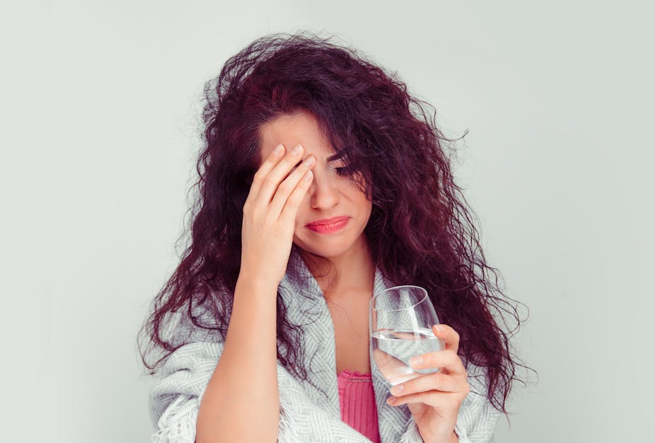 A woman with a hangover holds her head and a glass of water in her other hand.