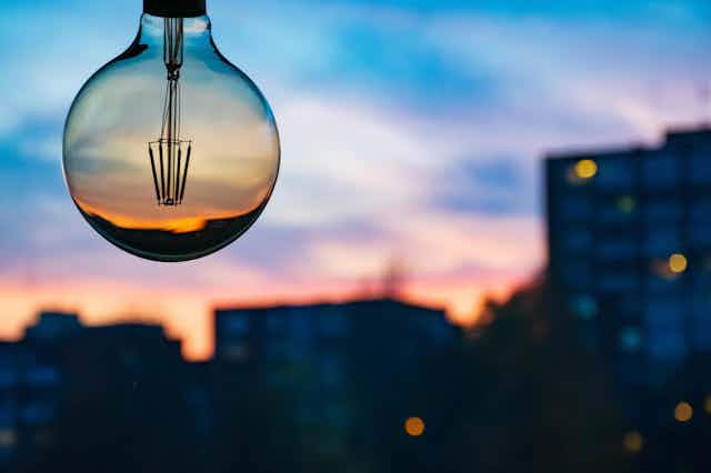 A defocused sunset over tower blocks with a lightbulb in the foreground.