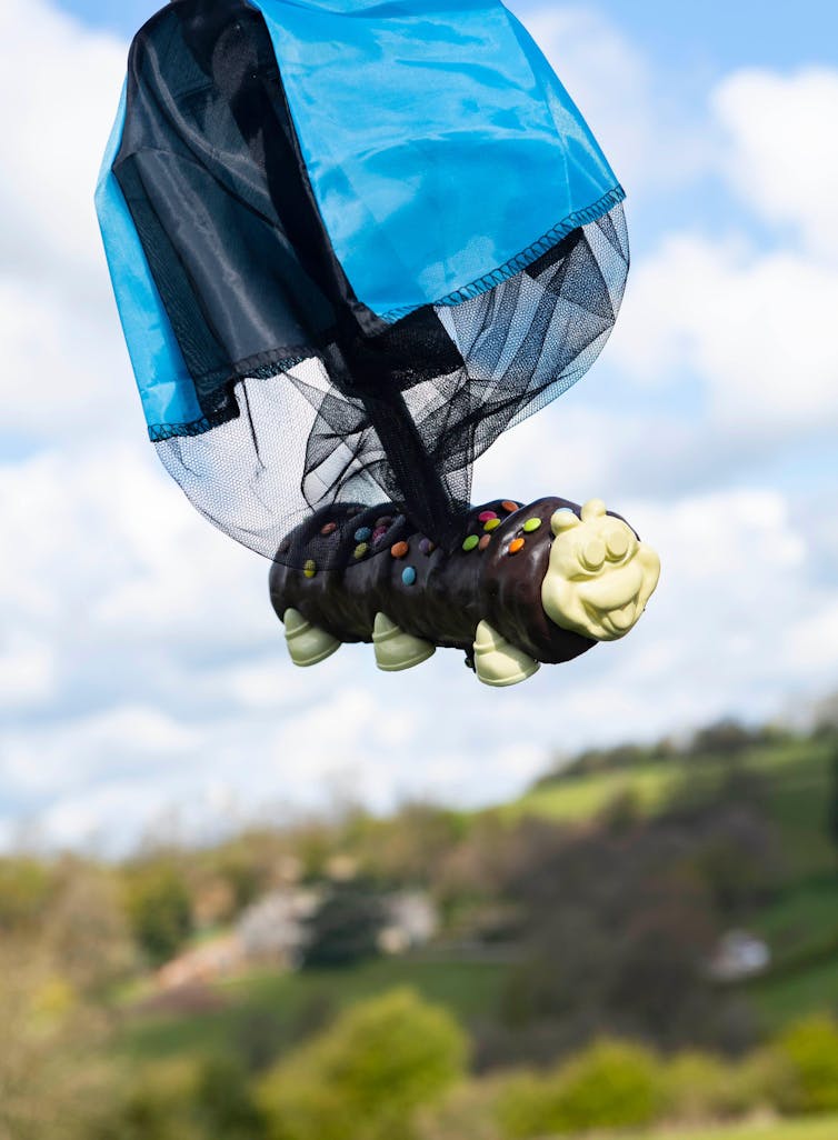 A chocolate cake in mid-air, attached to a blue and black parachute.
