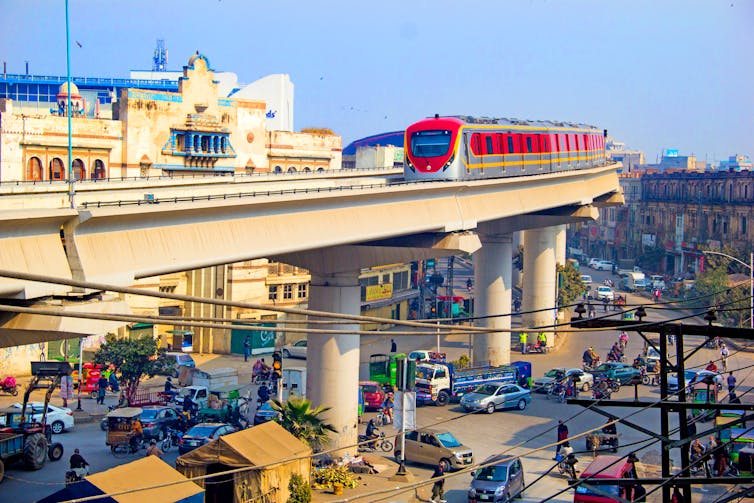 An orange metro train travels on an elevated rail in Lahore, Pakistan
