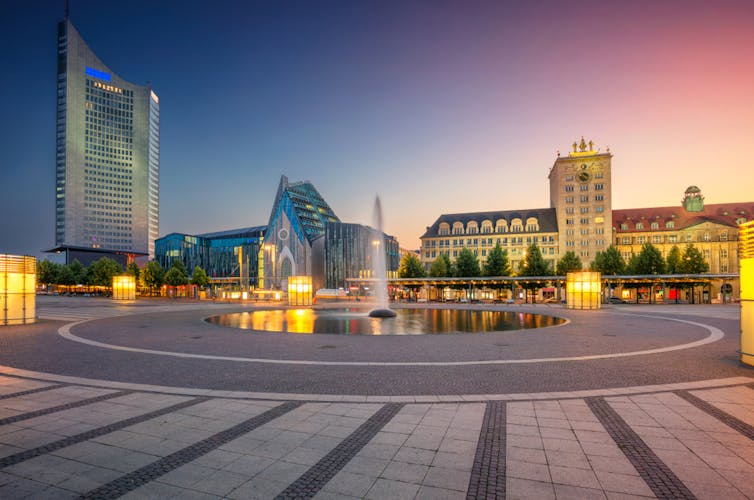 A public square at dusk with large fountain and modern and old buildings