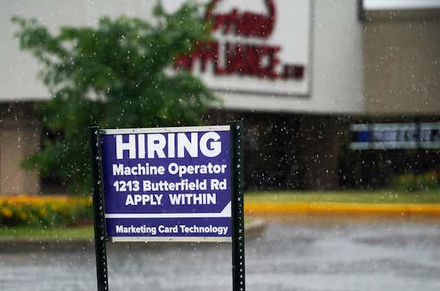A blue and white 'hiring' sign outside an appliance store..