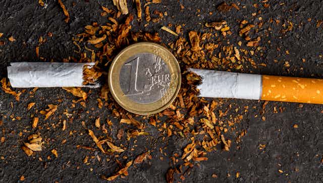 Moneda de euro en medio de un cigarrillo roto por la mitad.