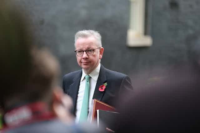 Levelling up secretary Michael Gove wearing a suit with a poppy on his lapel, walking with folders under his arm