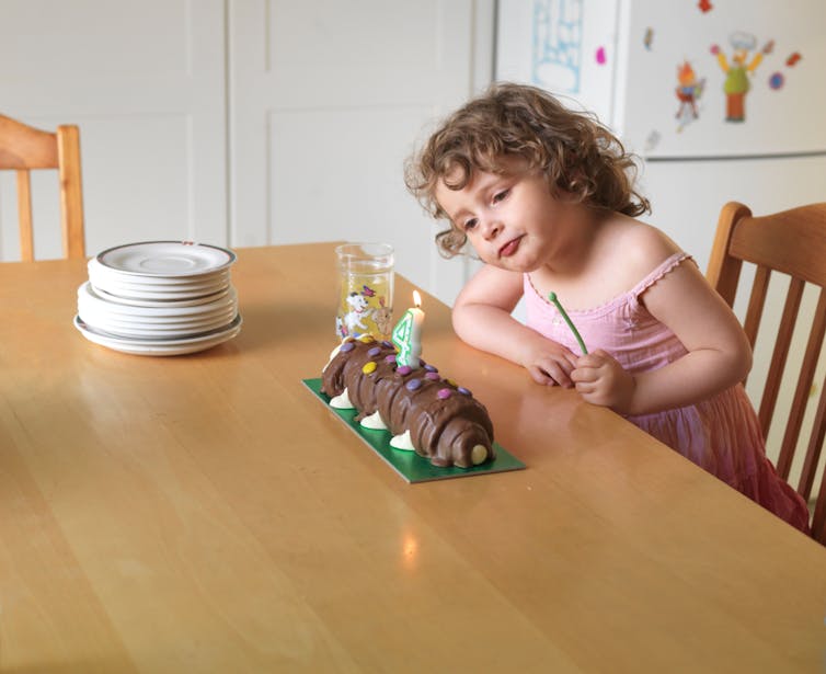 A little girls looks at a caterpillar birthday cake with candles.
