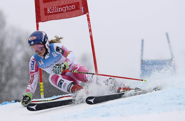 A woman making a tight turn on skis around a red gate.