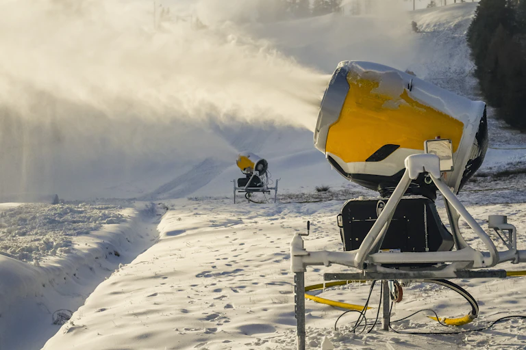 Two snowguns blowing snow onto a mountainside.