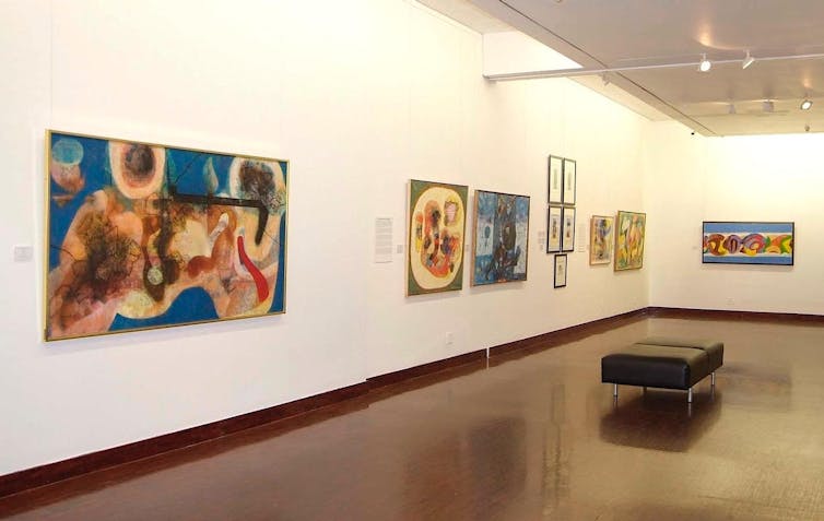 Paintings on gallery walls showing colourful, abstract forms and shapes.