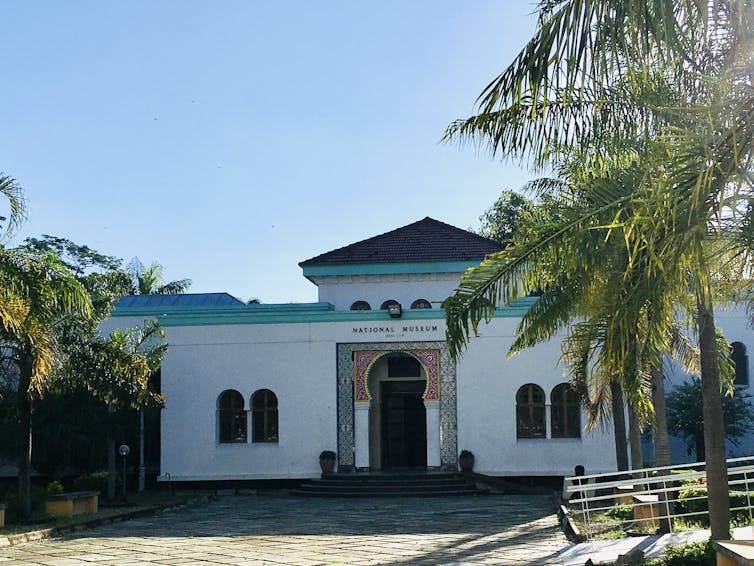 White and teal museum building surrounded by palm trees