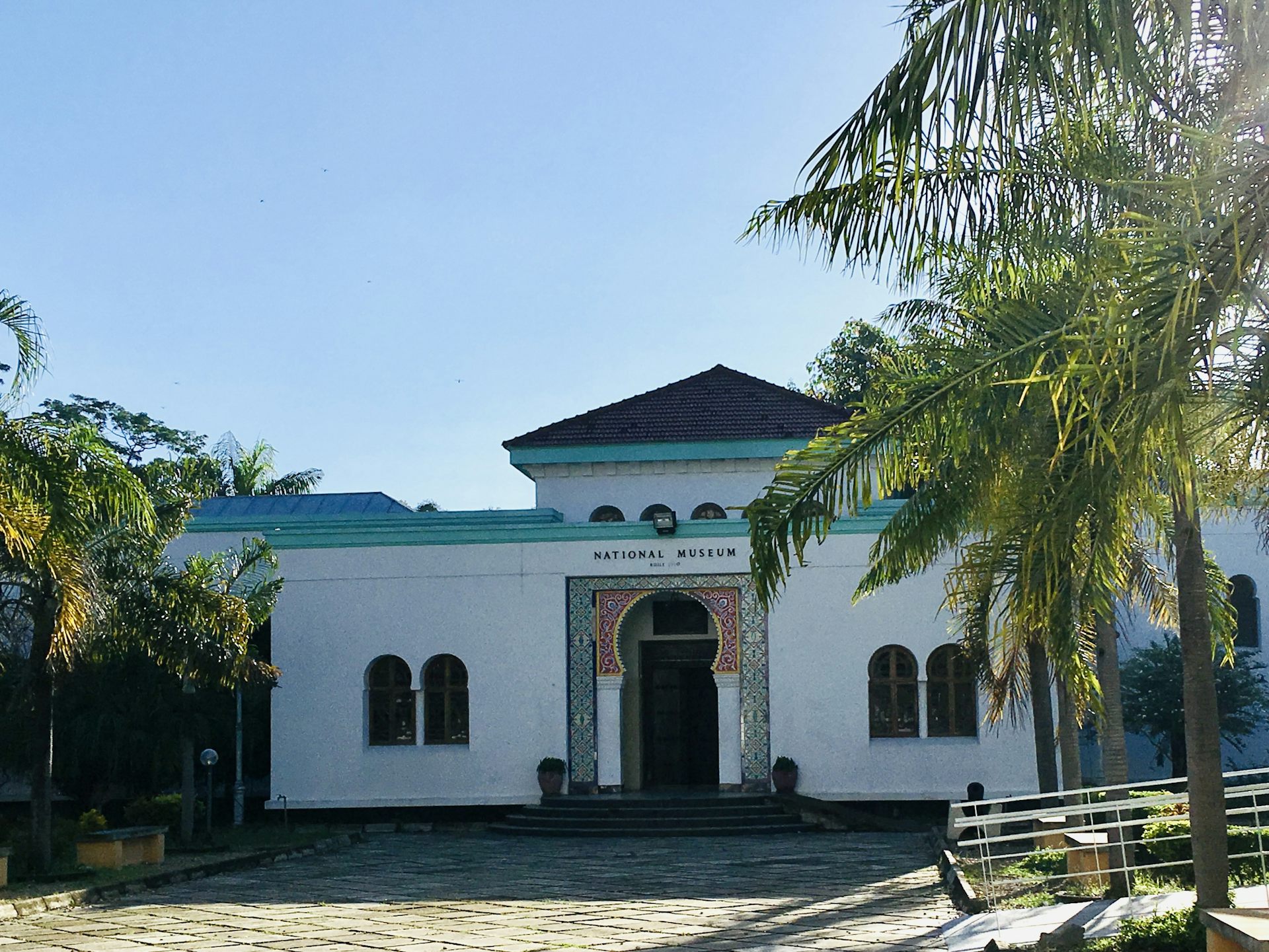 White and teal museum building surrounded by palm trees