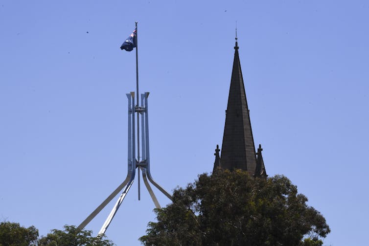A steeple in front of the Parliament House flag.