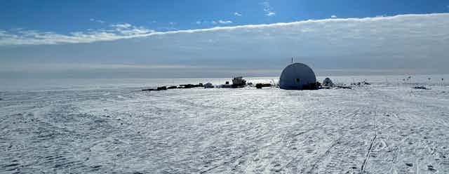 Large tent on an ice sheet with wide ice horizon and cloud bank.