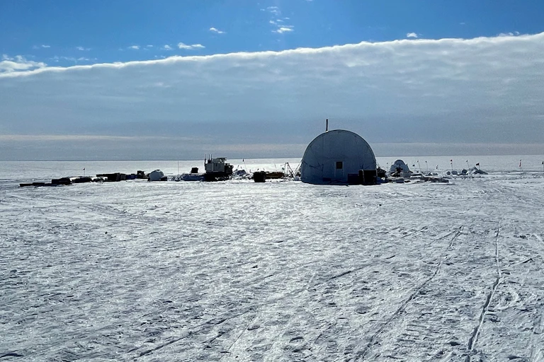 Large tent on an ice sheet with wide ice horizon and cloud bank.