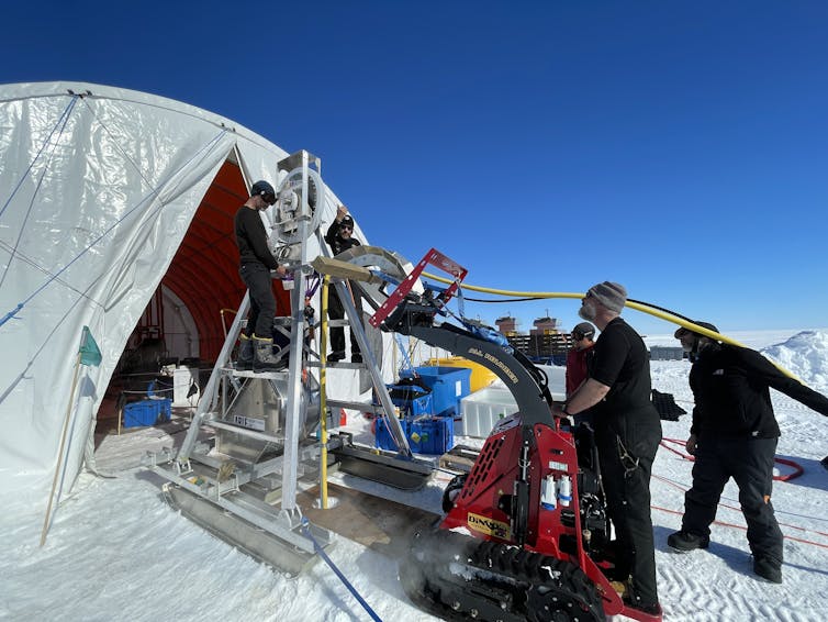 A group of engineers swarm around a frame to help lower equipment designed to melt a hole in the ice shelf.
