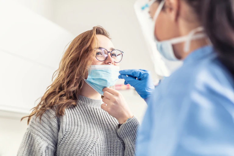 photo d’une soignante en blouse effectuant un prélévement nasal sur une femme.