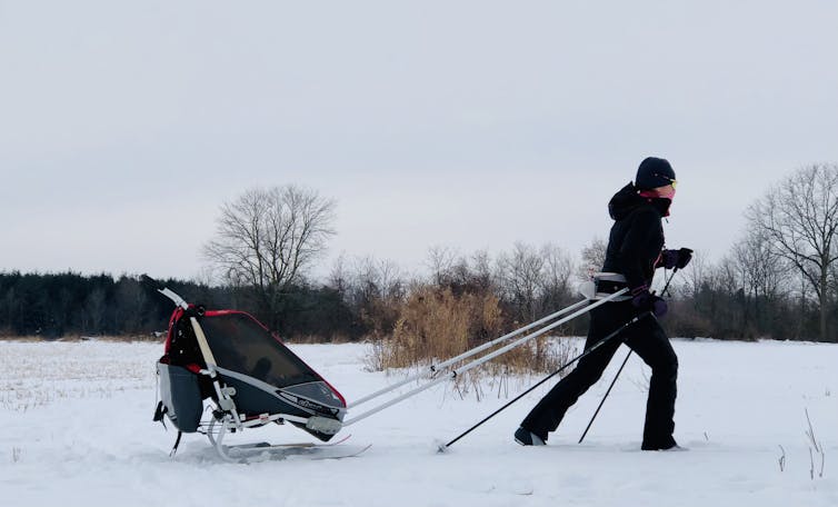 A woman walking through snow using Nordic poles and towing a sled.