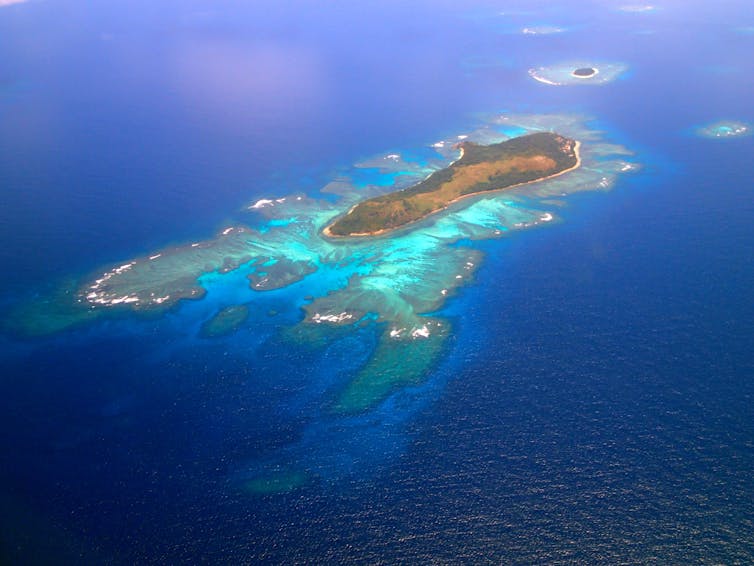 An aerial view of an island with white sand atolls and turquoise waters around it.