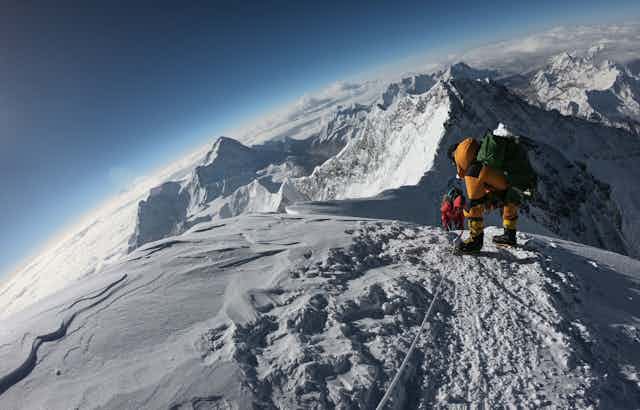A mountaineer on a peak overlooking snowy mountains and glaciers