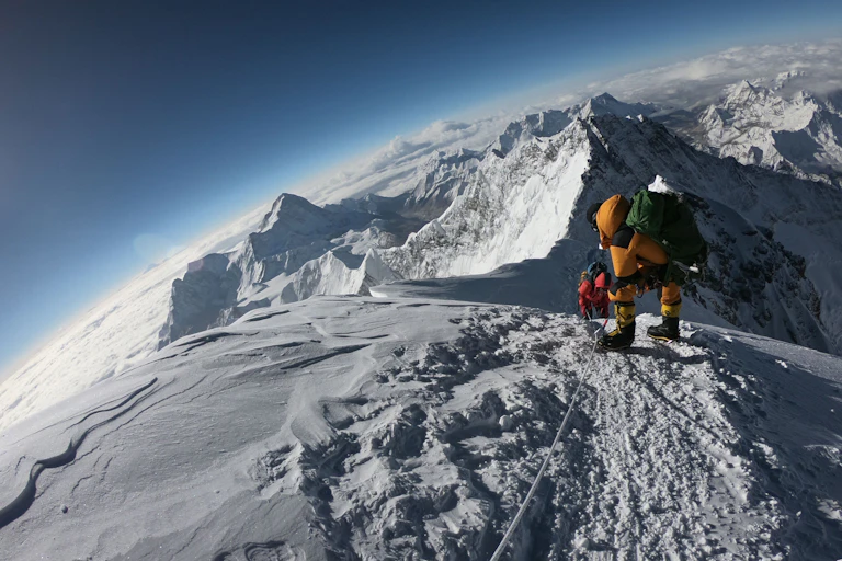 A mountaineer on a peak overlooking snowy mountains and glaciers