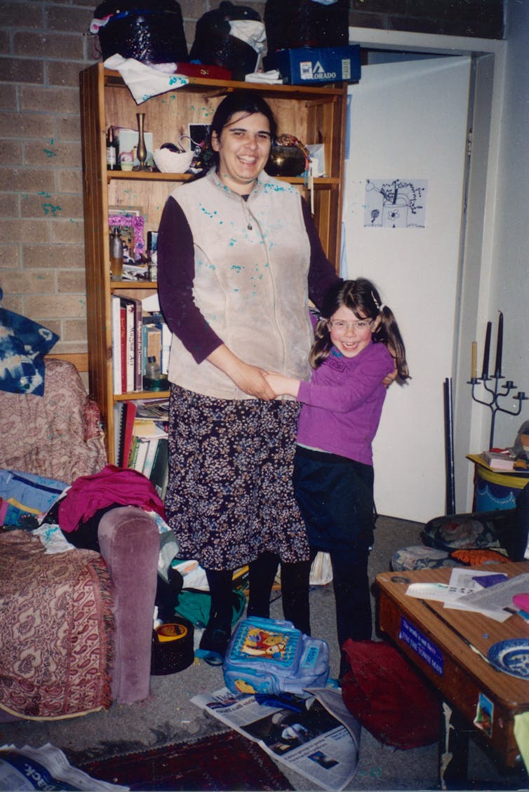 Woman with young daughter, standing affectionately entwined, together in living area.