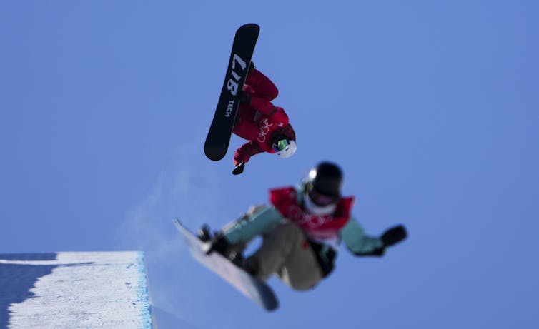 Two snowboarders in the air against a blue sky