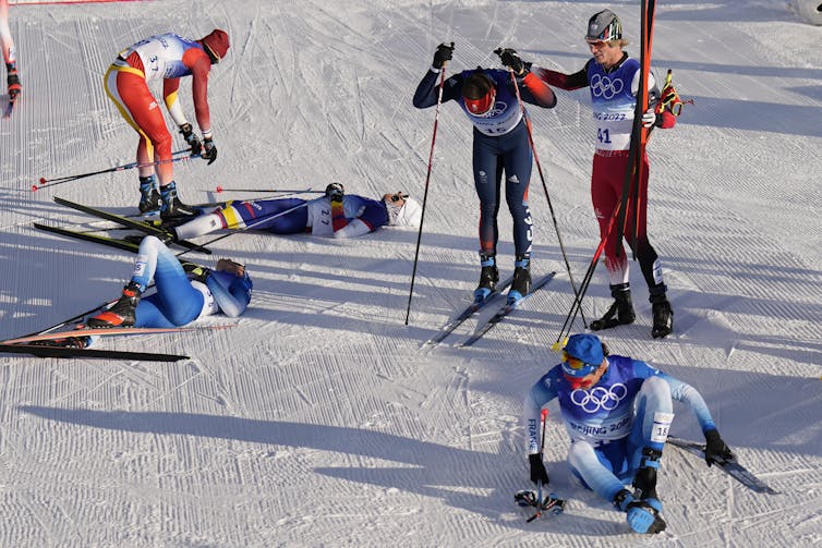 Three cross-county skiers collapsed on the snow after a race while three other skiers remain on their skis looking exhausted.