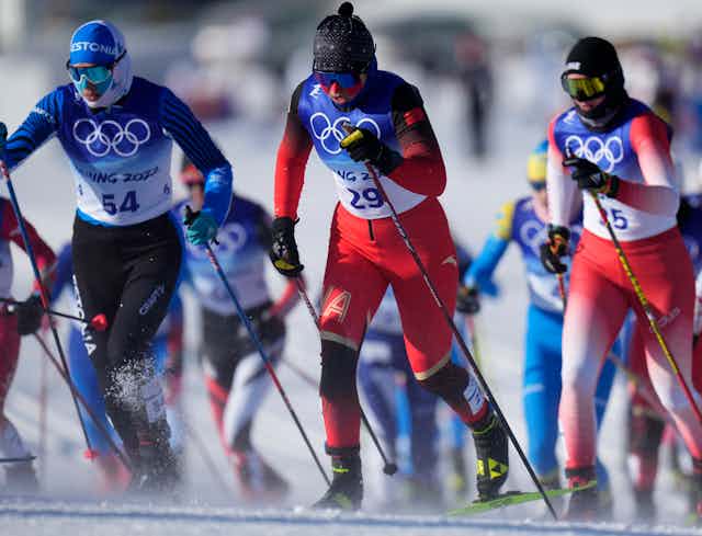 Three women cross-country skiers in the foreground with other competitors behind them