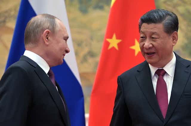 Russian president Vladimir Putin and Chinese president, Xi Jinping, smile at each other in front of Russian and Chinese flags.