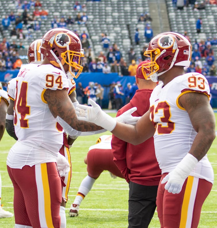 Two Washington American football players high five each other on the field during a game, the old Redskins logo is visible on their helmets